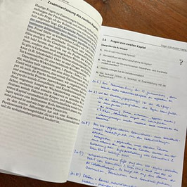 Buch: Einführung Ernährungspsychologie Aufgeschlagenes Buch mit einer Kapitelseite links und handschriftlichen Antworten zu Fragen auf der rechten Seite.