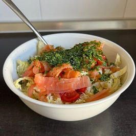 Mein Abendessen am Turbo-Fastentag Weiße Schüssel mit Salat aus Chinakohl, Tomaten, Räucherlachs und Kräutern auf einer Küchenarbeitsplatte.