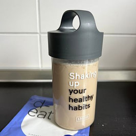 Meine Abkürzung am Turbo-Fastentag Ringana-Shaker mit beige-braunem Proteinshake und d-eat Pulverpackung auf einer Küchenarbeitsplatte.