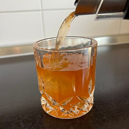 Ringana dea Shot wird ins Glas gegossen Nahaufnahme eines gold-orangefarbenen Getränks, das in ein kleines Kristallglas gegossen wird.