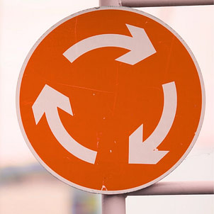 Denkfehler 2 – Disziplin ist der Schlüssel Orangefarbenes Verkehrsschild mit kreisenden Pfeilen – Symbol für den endlosen Kreislauf aus Disziplin, Verzicht und Rückfall beim Abnehmen