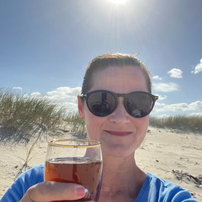 In_12_Tagen_zu_mehr_Leichtigkeit_2024_Sandown_Bay Sonja Fuchs alias Fuchsmunter mit einem Glas Ringana dea am Strand in Südafrika.