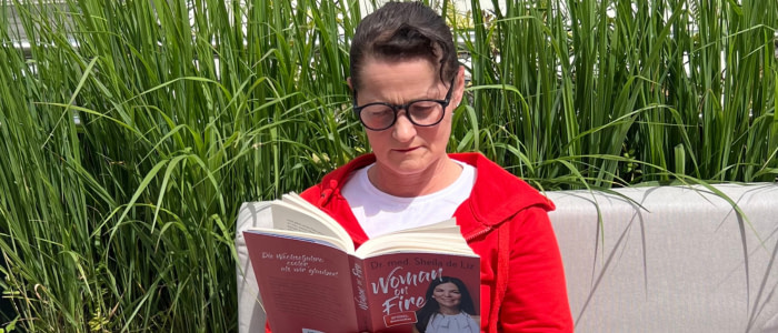 Sonja Fuchs alias Fuchsmunter in dreifacher Ausführung auf dem Balkon. Sie liest das Buch Woman on Fire.